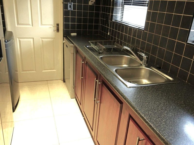 A functional scullery area featuring dark tiled splashbacks, laminate countertops, and a double stainless steel sink with built-in cabinetry.
