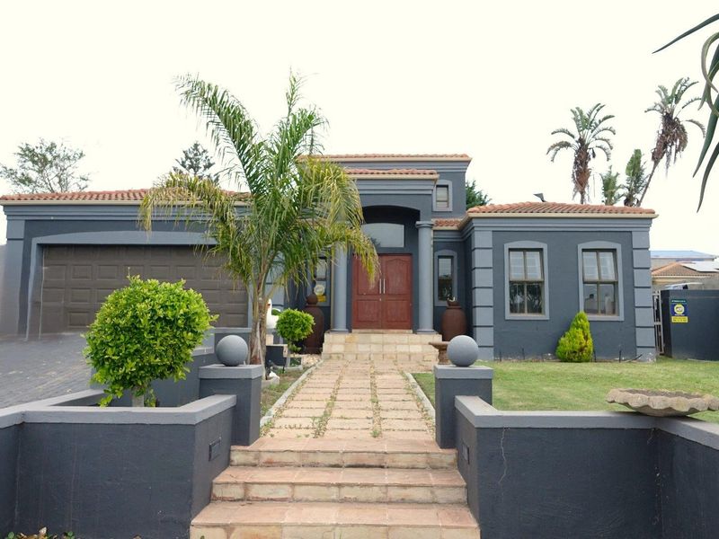 Front elevation of a modern house featuring a double garage, paved walkway, and a prominent entrance with stone pillars.