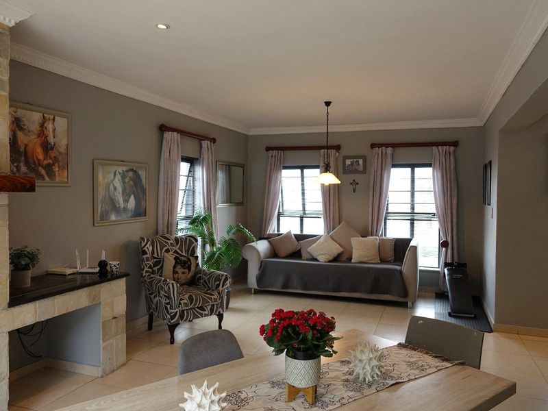 A spacious living room featuring a stone-clad fireplace, tiled flooring, crown molding, and recessed lighting, creating a comfortable and well-maintained living environment.