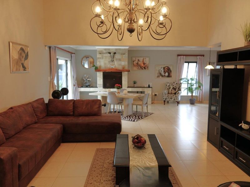 Spacious open-plan living and dining area featuring tiled floors, a prominent stone fireplace, and a high ceiling with a decorative chandelier.