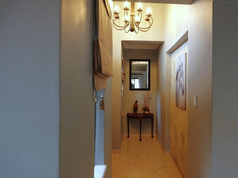 A well-lit hallway featuring tiled flooring, a decorative chandelier, and a textured feature wall.