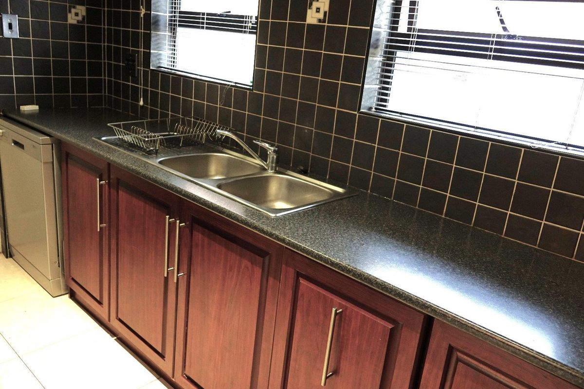 A functional kitchen area featuring dark wood cabinetry, granite-style countertops, a double stainless steel sink, and dark tiled splashbacks.