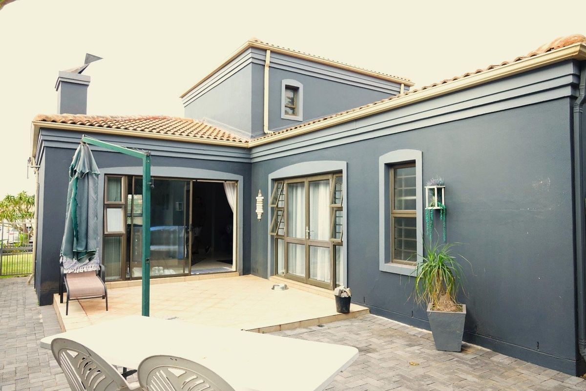 Rear exterior view of the house featuring a paved patio area, sliding glass doors, and dark grey painted exterior walls with terracotta roof tiles.