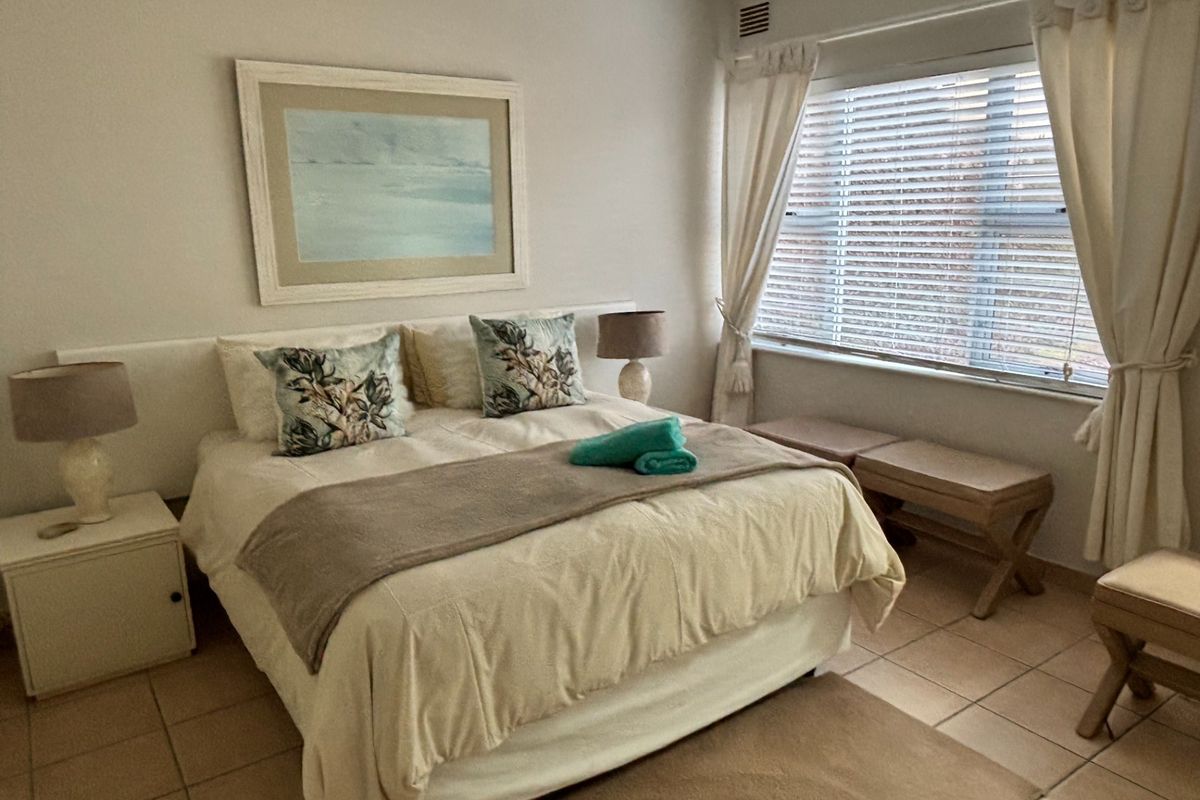 A well-lit bedroom featuring tiled flooring, a large window with blinds, and a neutral color palette.
