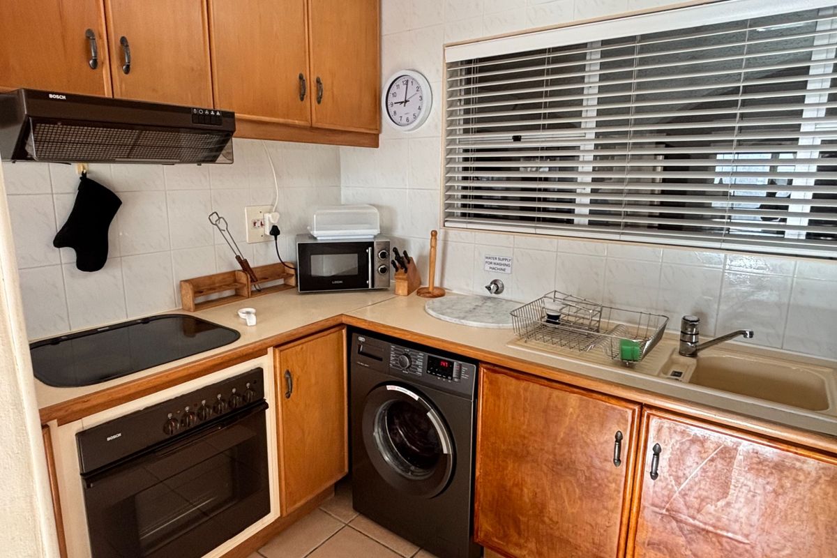 Functional kitchen featuring wood-finish cabinetry, integrated oven, hob, extractor fan, and a dedicated space for a washing machine under the counter.