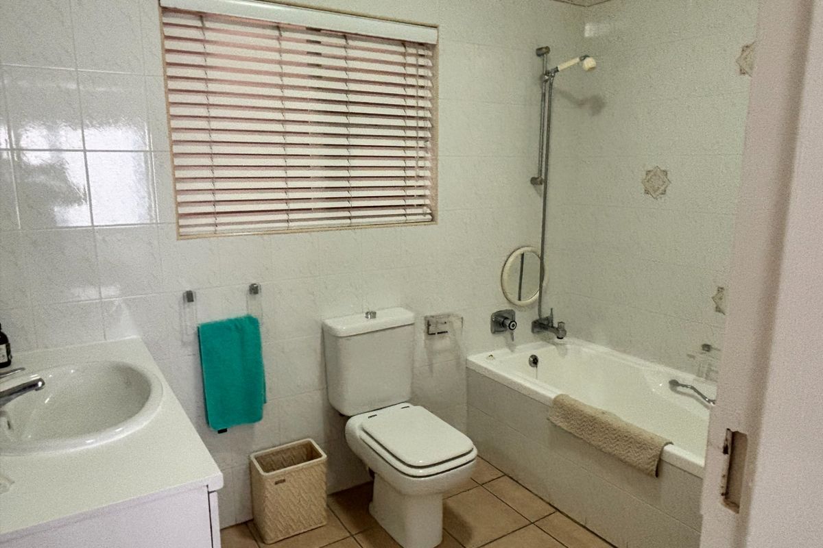 A functional bathroom featuring a built-in bathtub with shower attachment, a vanity basin, and a toilet, finished with neutral wall and floor tiles.