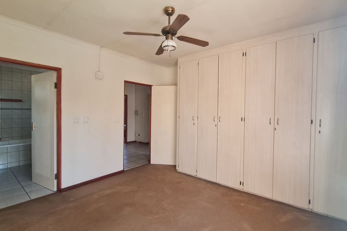 Spacious bedroom featuring extensive built-in cupboards, a ceiling fan, and direct access to an ensuite bathroom with tiled flooring.