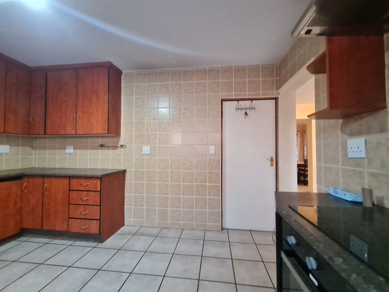 A functional kitchen featuring wooden cabinetry, tiled splashbacks, tiled flooring, and built-in cooking appliances, offering a clean and practical workspace.