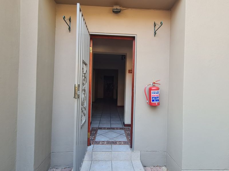 Entrance area featuring a security gate, tiled flooring, and a wall-mounted fire extinguisher, providing access to the interior hallway.