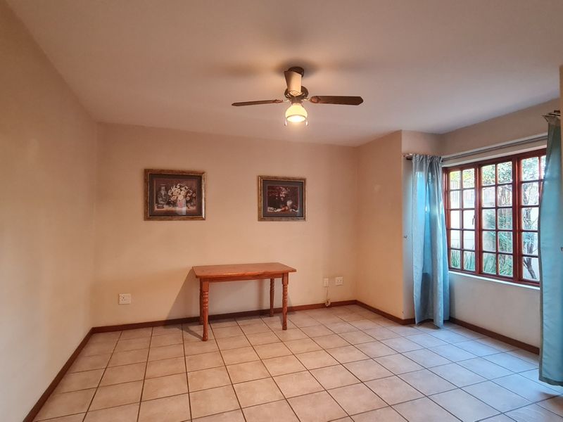 A living area featuring tiled flooring, a ceiling fan, and wooden window frames, offering a neutral space ready for personalization.
