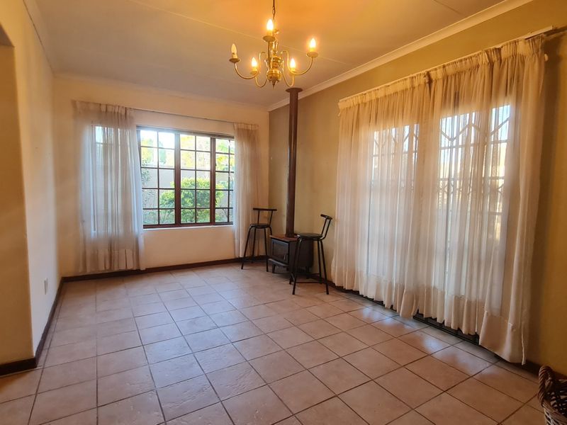 Spacious living area featuring tiled flooring, a central freestanding fireplace, and large windows providing natural light and garden access.