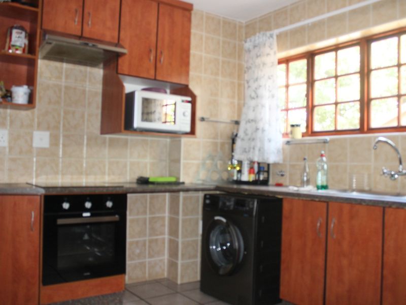 A functional kitchen featuring wooden cabinetry, tiled backsplash, built-in oven with extractor fan, and a stainless steel sink under a window.