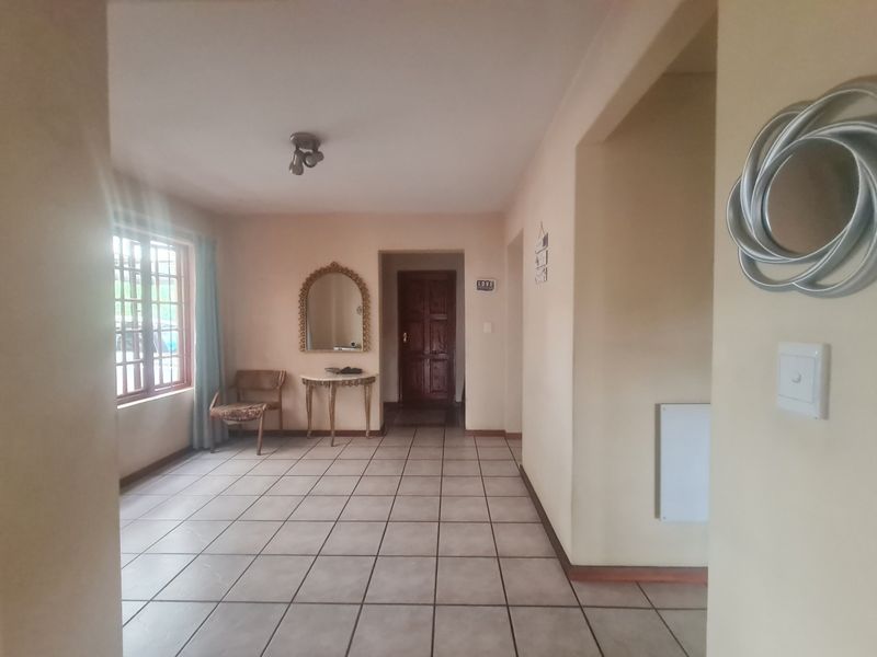 A spacious living area featuring neutral tiled flooring, a timber-framed window, and a solid timber entrance door, offering a functional and well-lit layout.