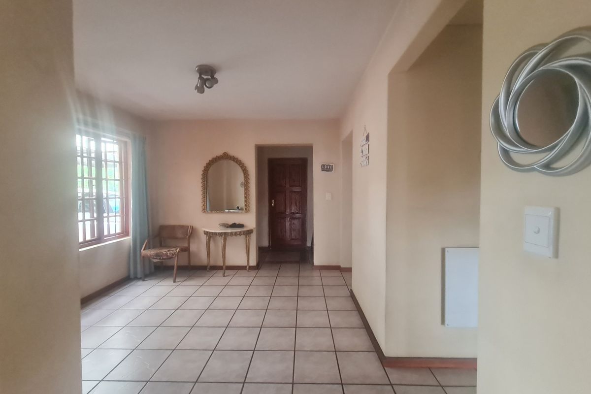 A spacious living area featuring neutral tiled flooring, a timber-framed window, and a solid timber entrance door, offering a functional and well-lit layout.