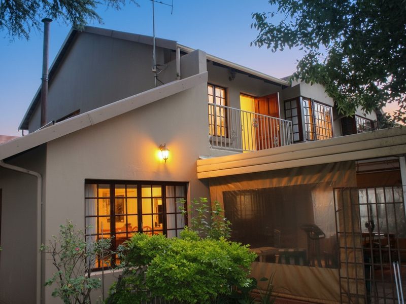 Rear view of the townhouse featuring a covered patio area, a balcony with metal railing, and exterior lighting at dusk.