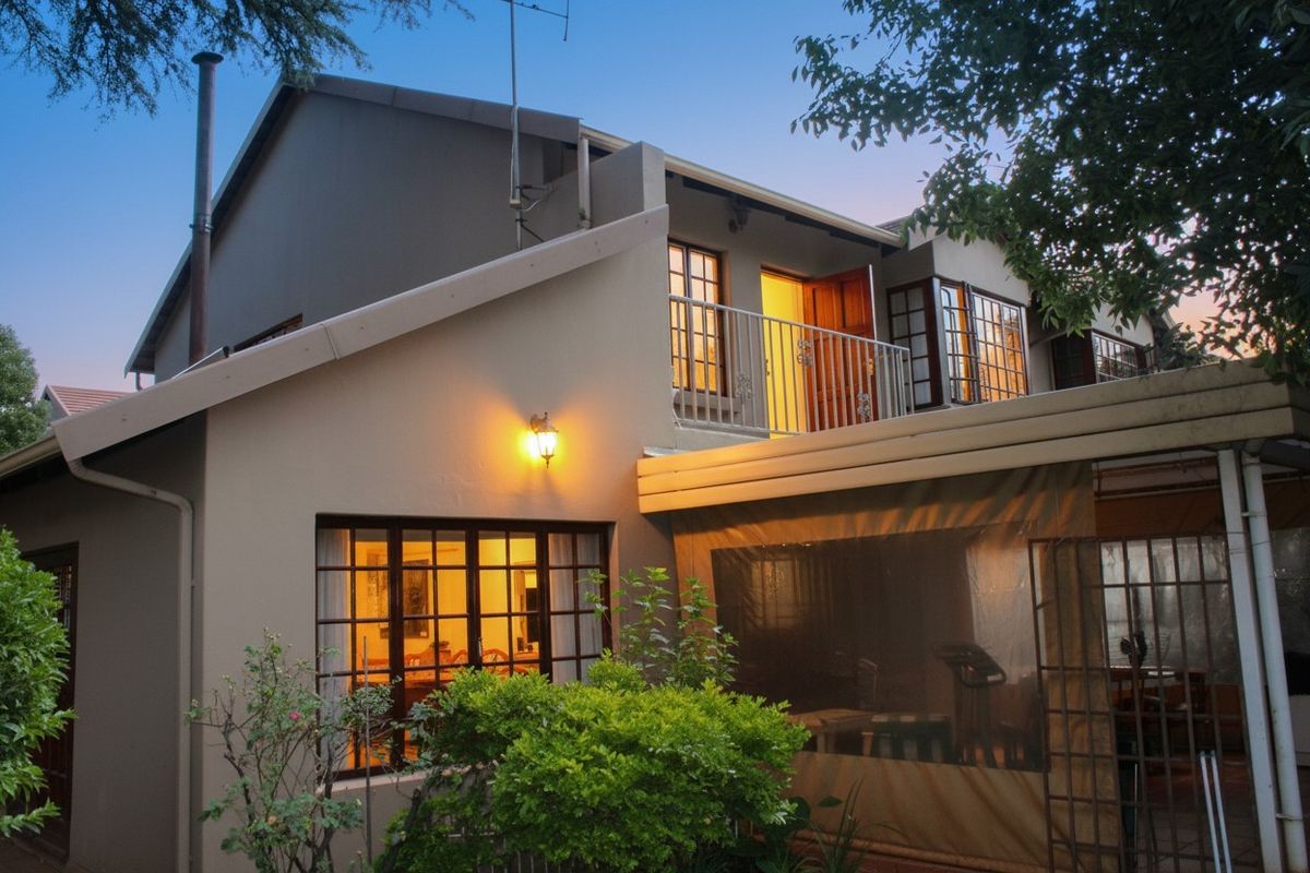 Rear view of the townhouse featuring a covered patio area, a balcony with metal railing, and exterior lighting at dusk.