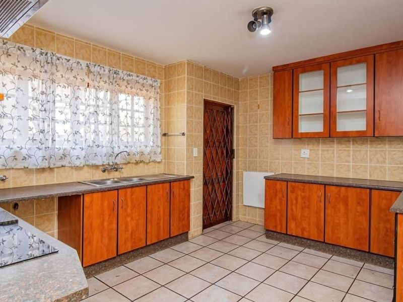 A functional kitchen featuring wood-look cabinetry, laminate countertops, tiled backsplash, and flooring, equipped with a built-in hob and extractor fan.