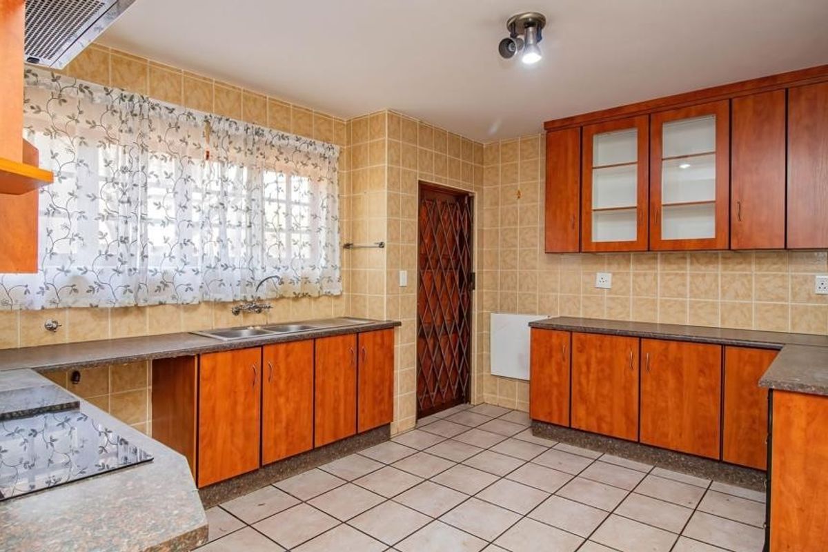 A functional kitchen featuring wood-look cabinetry, laminate countertops, tiled backsplash, and flooring, equipped with a built-in hob and extractor fan.