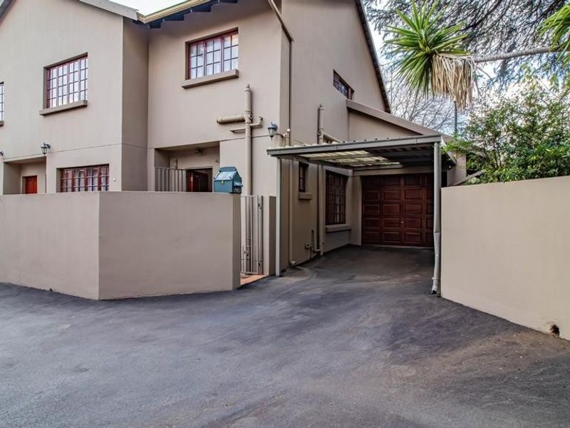 Front exterior view of a townhouse featuring a paved driveway, a covered carport, and a secure boundary wall with a private entrance.