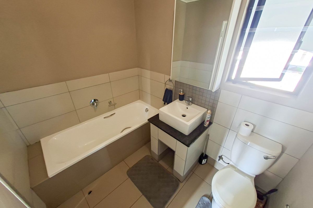 A functional bathroom featuring a built-in bathtub, a modern vessel sink vanity, a wall-mounted mirror, and a standard toilet.