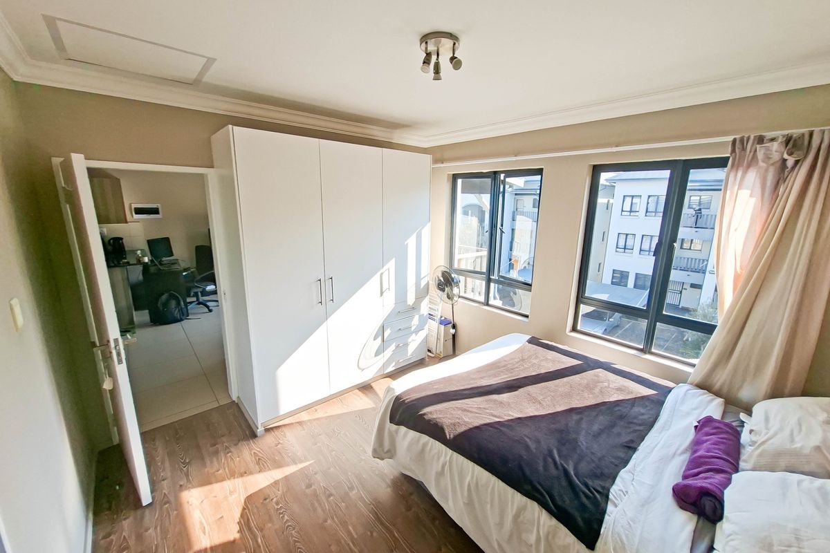 A bedroom featuring wood-look flooring, built-in white cabinetry, and large windows providing natural light and views of the surrounding apartment complex.