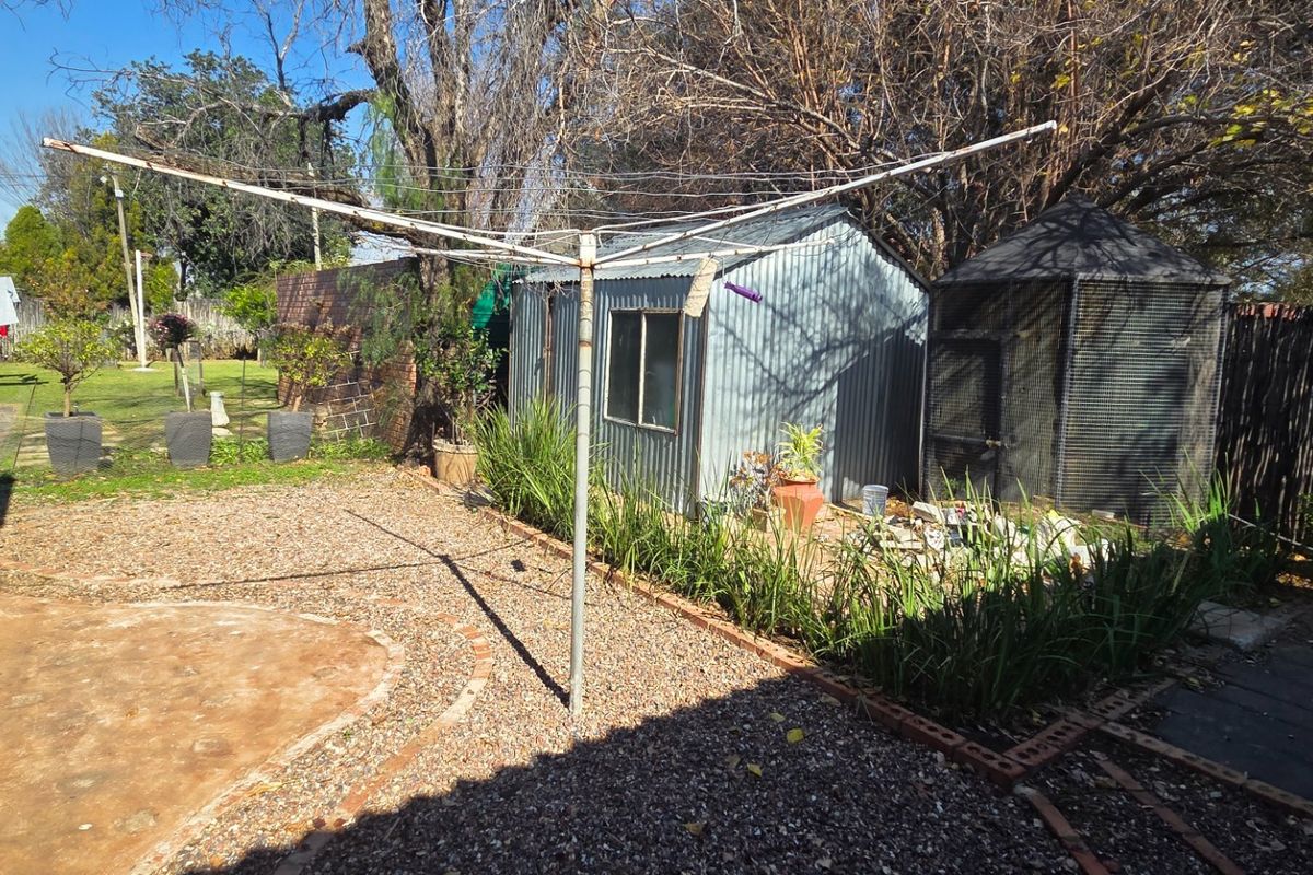 A spacious rear garden area featuring a metal storage shed, gravel landscaping, and a rotary clothesline, offering potential for outdoor improvement.