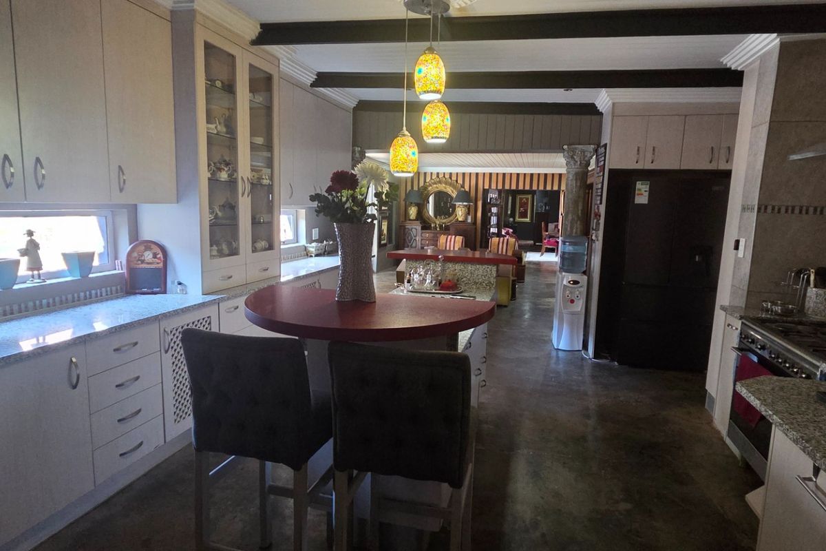Spacious kitchen featuring extensive built-in cabinetry, granite countertops, gas hob with extractor, and exposed ceiling beams, flowing into an open-plan living area.