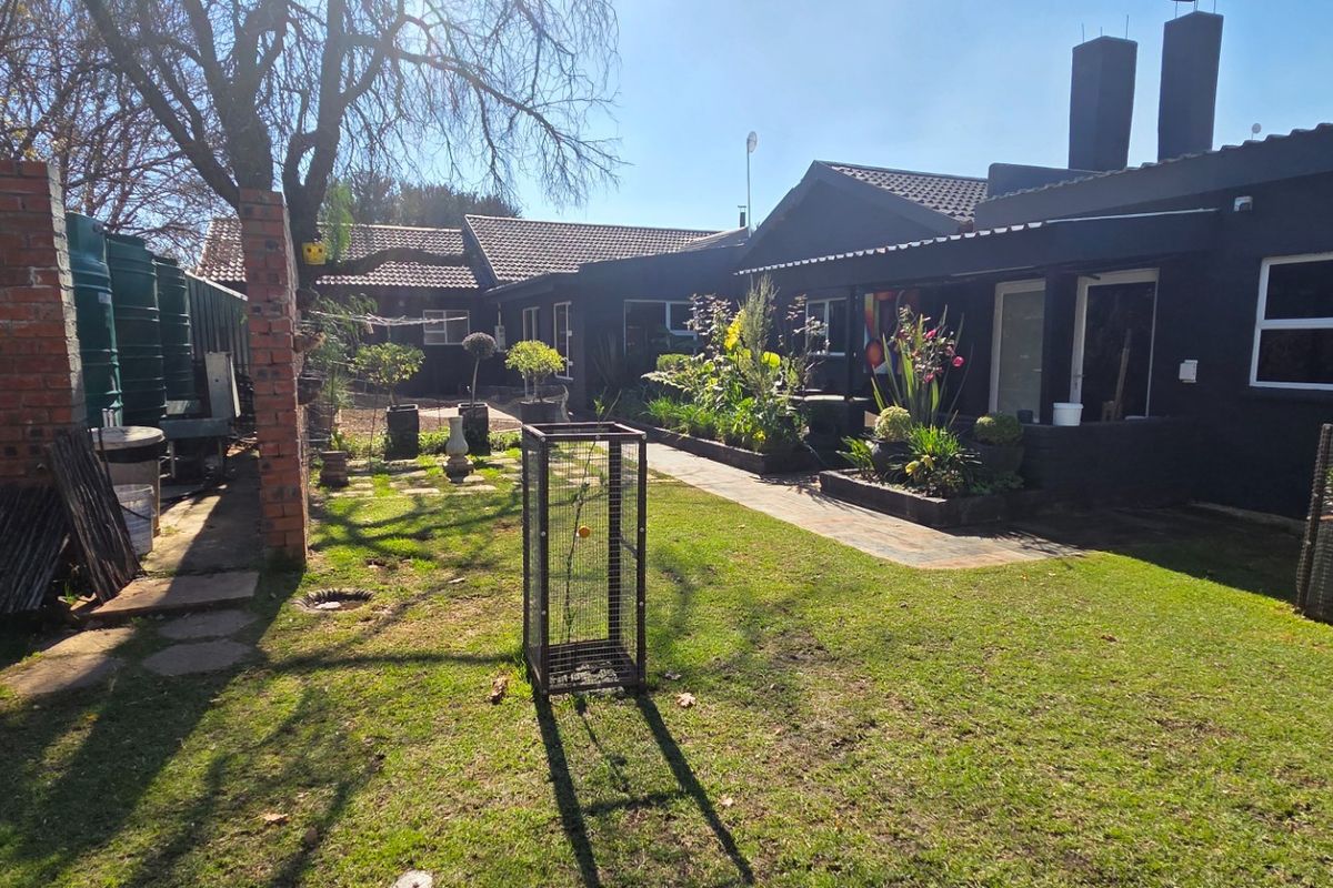 A rear garden view featuring a lawn, paved walkway, raised garden beds, and water storage tanks against the dark-painted exterior of the house.