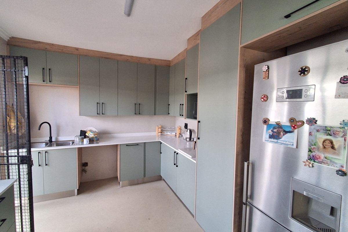 Modern kitchen featuring sage green cabinetry, light wood-look trim, white countertops, and integrated appliance housing.