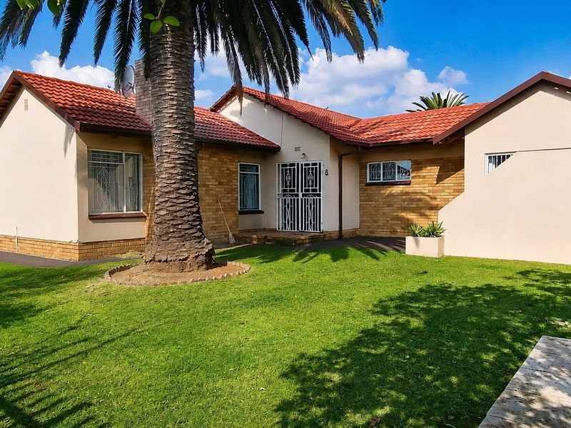 Front view of a single-story house featuring a tiled roof, brick and plaster facade, and a well-maintained front lawn with a mature palm tree.