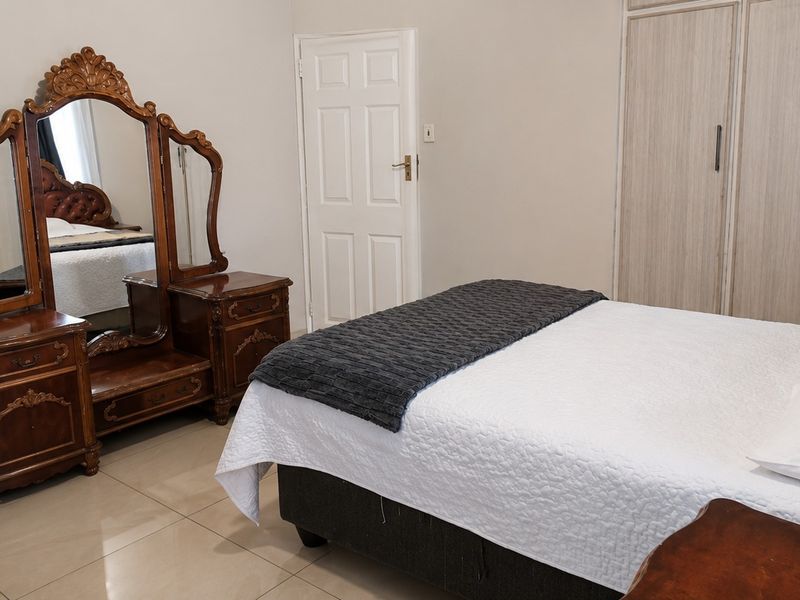 A well-maintained bedroom featuring neutral tiled flooring, built-in cupboards, and a classic panel door.
