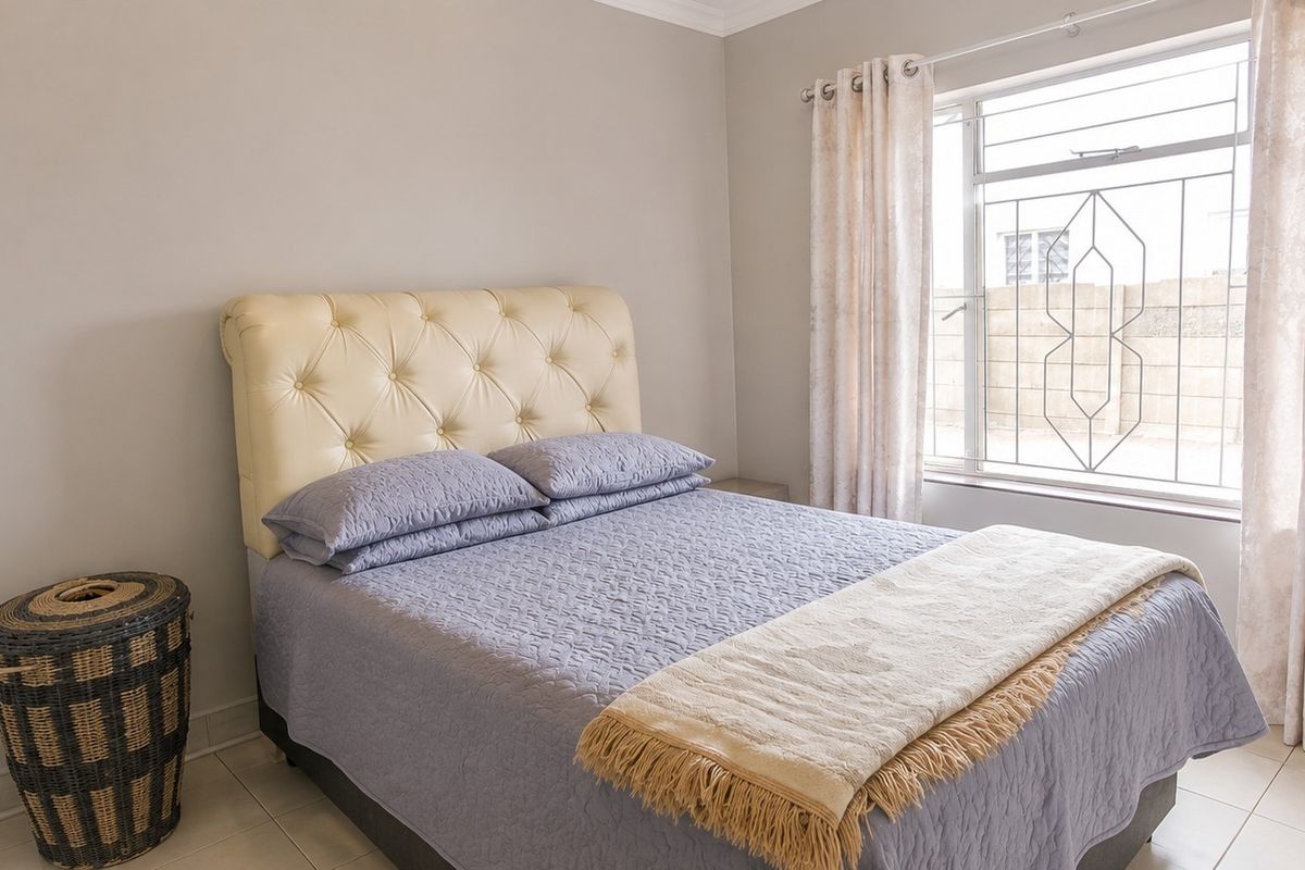 A well-maintained bedroom featuring neutral wall tones, tiled flooring, and a window fitted with security bars.