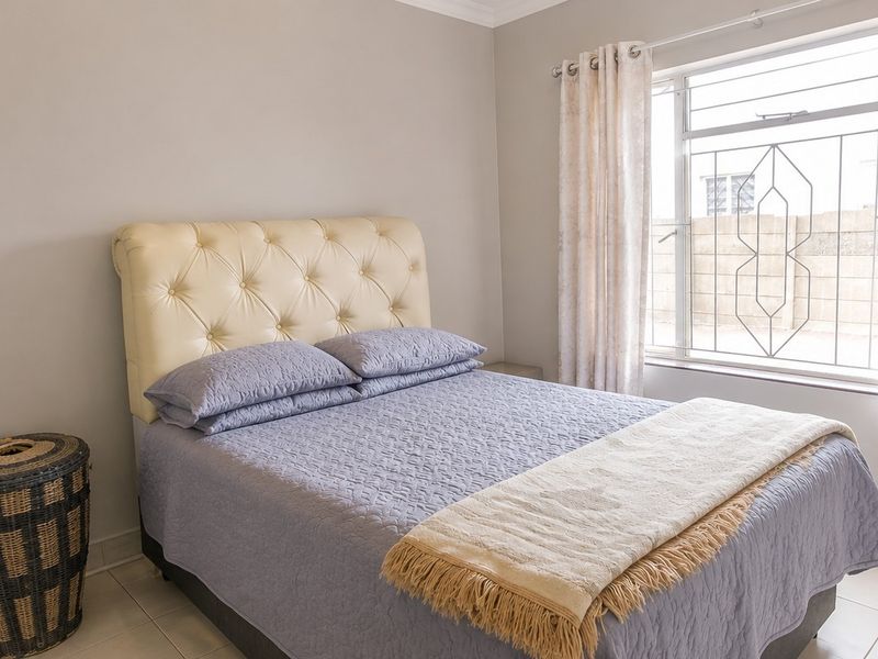 A well-maintained bedroom featuring neutral wall tones, tiled flooring, and a window fitted with security bars.