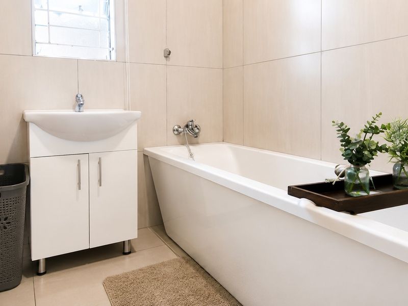 A clean, modern bathroom featuring neutral wall tiles, a white vanity cabinet with a basin, and a standard bathtub with chrome fixtures.