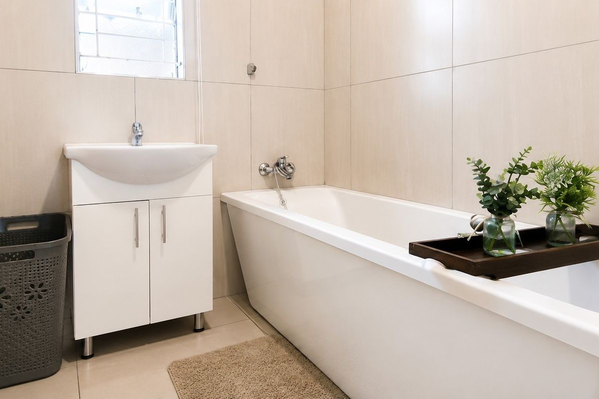 A clean, modern bathroom featuring neutral wall tiles, a white vanity cabinet with a basin, and a standard bathtub with chrome fixtures.