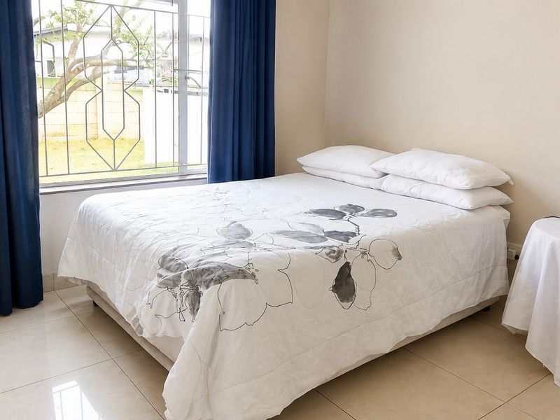 A well-maintained bedroom featuring neutral tiled flooring and a window fitted with security bars.
