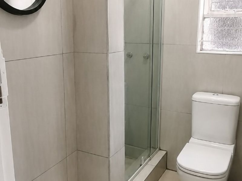 A clean, modern bathroom featuring neutral wall and floor tiles, a glass-enclosed shower, and a standard toilet.