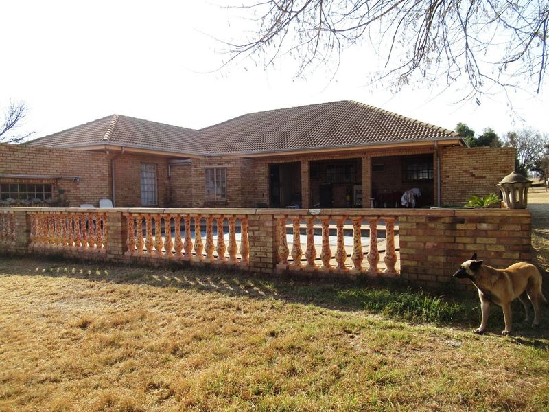 Rear view of a face-brick small holding residence featuring a covered patio area and a decorative balustrade wall overlooking the garden.