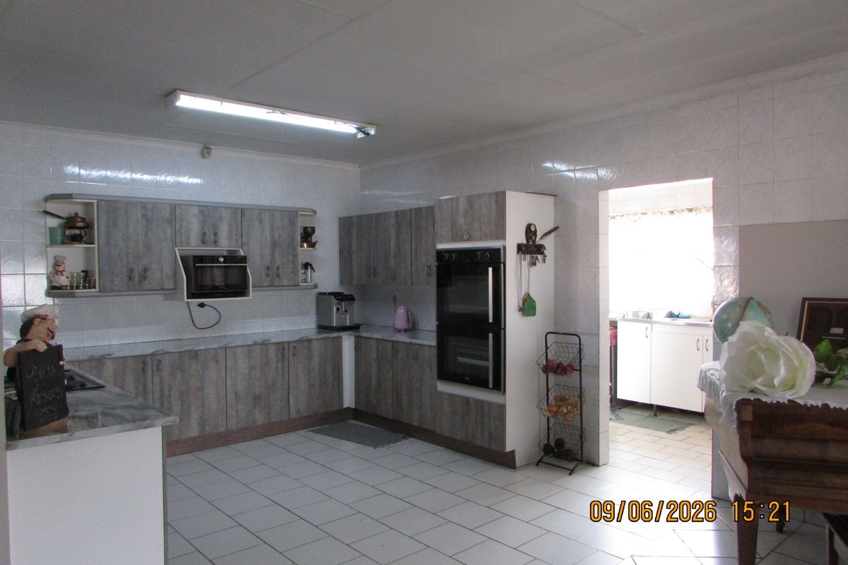 A functional kitchen featuring wood-look cabinetry, built-in double oven, and tiled flooring, with an adjacent scullery area.