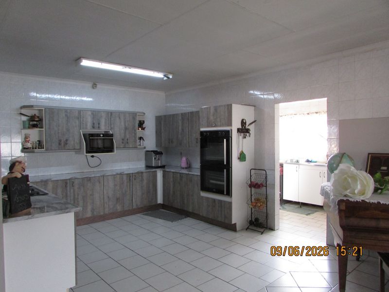 A functional kitchen featuring wood-look cabinetry, built-in double oven, and tiled flooring, with an adjacent scullery area.