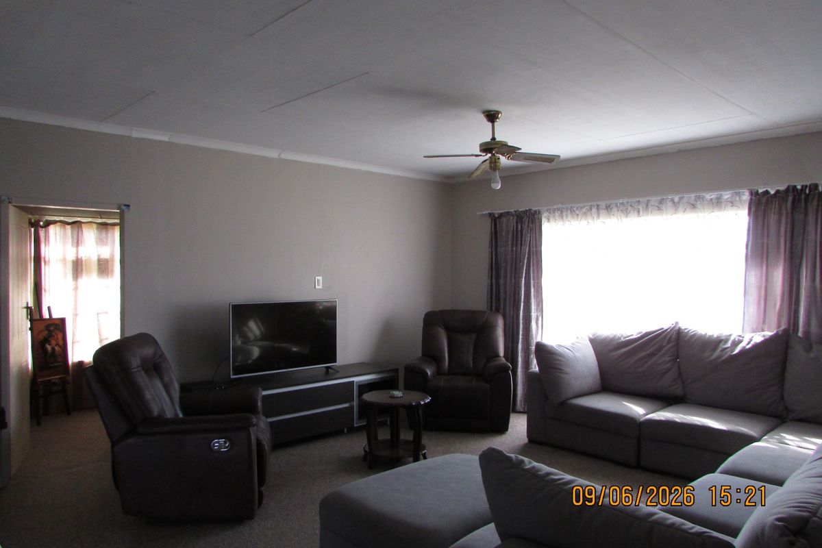 A spacious living room featuring neutral wall tones, carpeted flooring, and a ceiling fan, providing a comfortable and functional family living area.