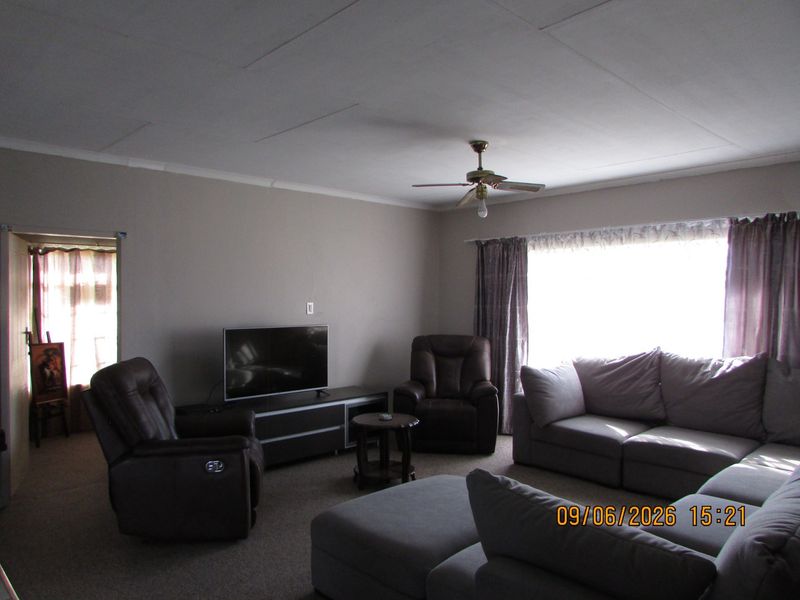 A spacious living room featuring neutral wall tones, carpeted flooring, and a ceiling fan, providing a comfortable and functional family living area.
