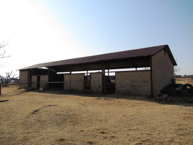 A large, open-sided agricultural outbuilding or stable structure featuring concrete block walls and a corrugated metal roof, situated on a rural small holding.