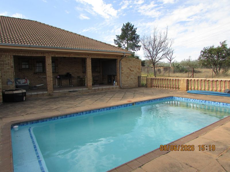 Outdoor entertainment area featuring a covered patio, paved pool deck, and a swimming pool with a balustrade surround.