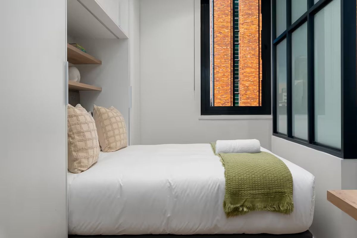 A compact bedroom featuring built-in cabinetry with integrated shelving and a large window providing natural light.