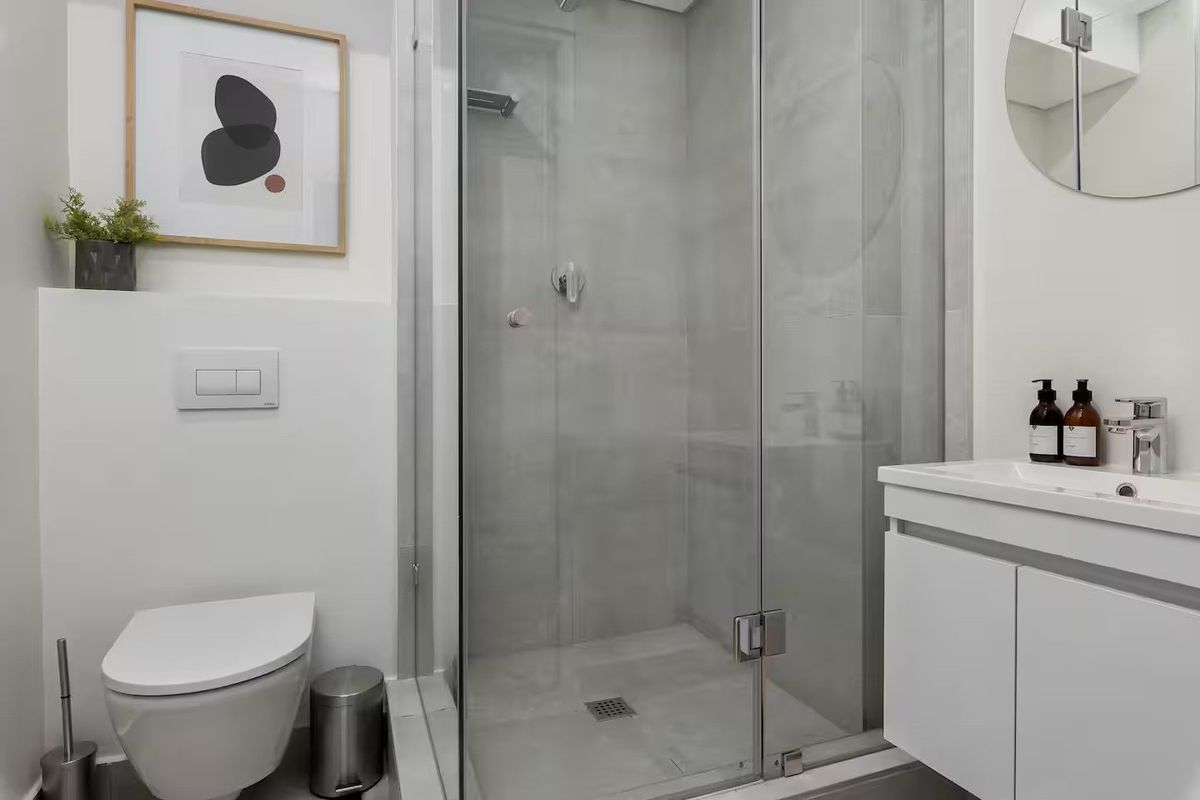 A modern, compact bathroom featuring a glass-enclosed shower, wall-mounted toilet, and a sleek vanity unit with a basin.
