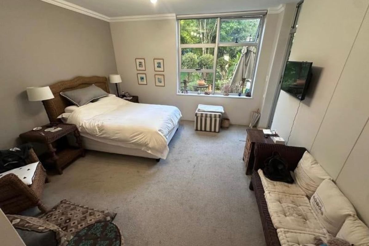 Spacious bedroom featuring large windows with garden views, crown molding, and wall-mounted television connectivity.