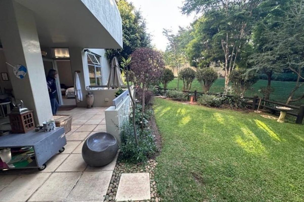 A spacious covered patio overlooking a well-maintained private garden with lush lawn and mature trees.