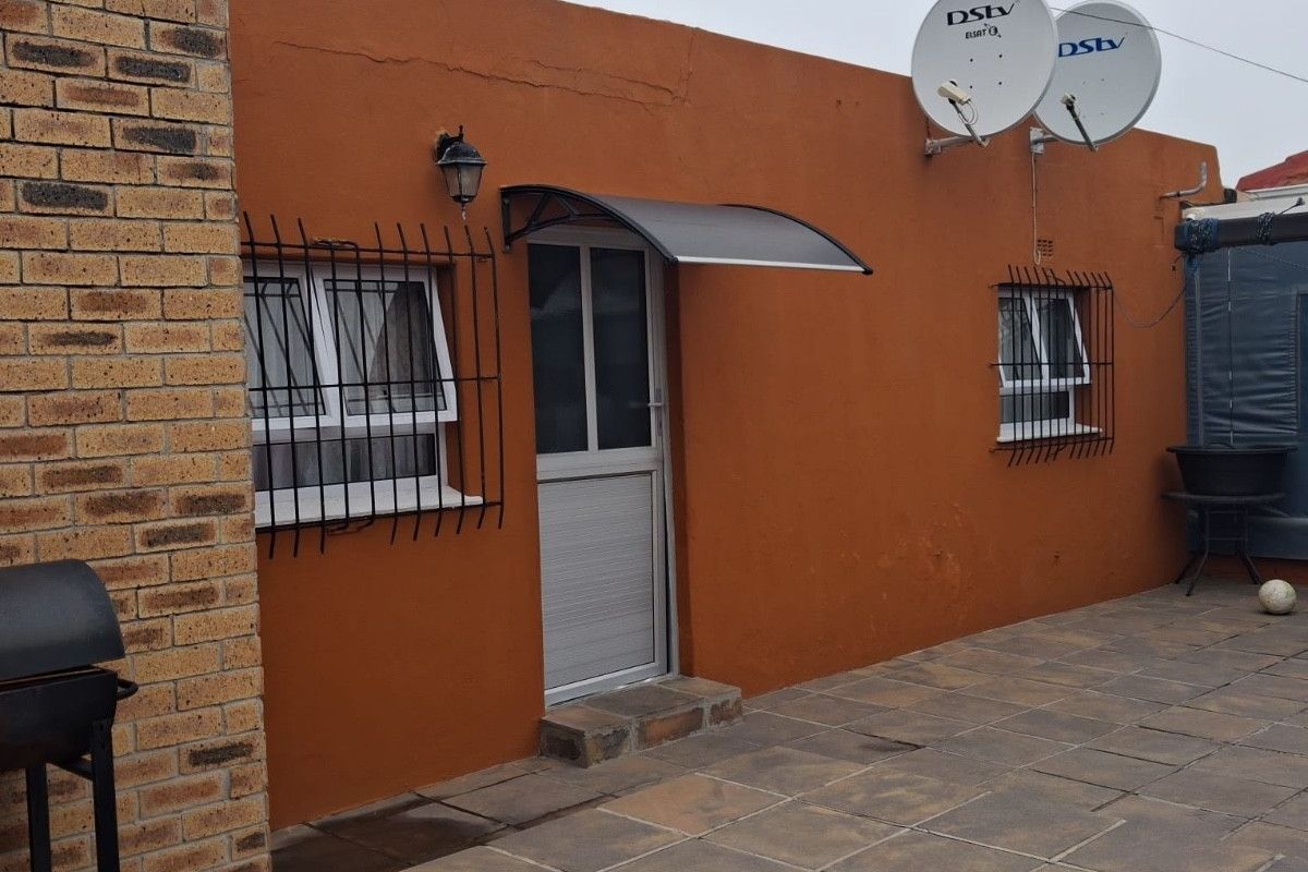 Rear exterior view of the property featuring a paved patio area, brick facade, security bars on windows, and mounted satellite dishes.