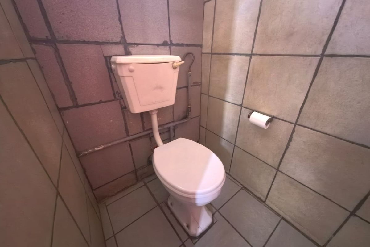 A compact bathroom featuring a standard toilet with a high-level cistern and full-height wall tiling.